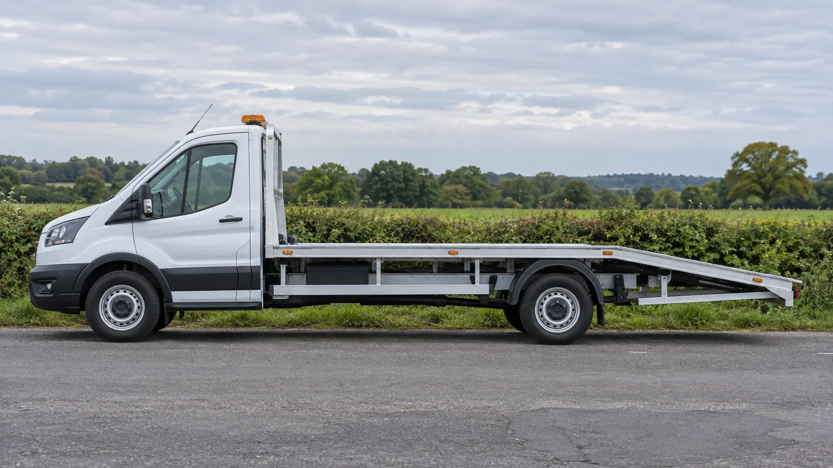 Unbranded white Ford Transit-style flatbed recovery truck on a UK countryside roadside